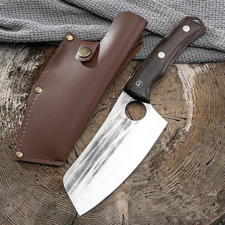 Hand-forged cleaver knife with wooden handle and leather sheath on rustic wood surface