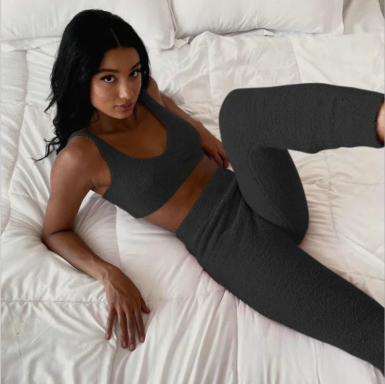 Woman in dark grey textured lounge set with crop top and high-waisted leggings on bed