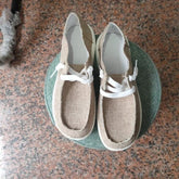 Beige canvas slip-on shoes with white laces and rubber soles on a green round stool