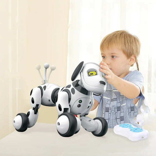 Child in light blue graphic t-shirt playing with a robot dog toy at a table indoors