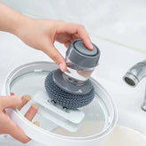 Hand cleaning glass pot lid with gray dish scrubber and soap dispenser