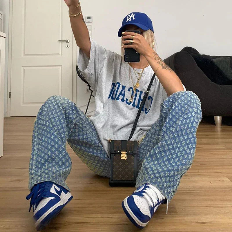Casual streetwear outfit with oversized gray graphic t-shirt, blue patterned loose pants, and blue-white sneakers.