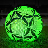Glowing neon green soccer ball with black geometric patterns on grass at night