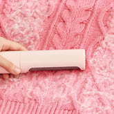 Hand removing lint from pink cable knit sweater with a fabric shaver