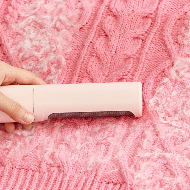 Hand removing lint from pink cable knit sweater with a fabric shaver