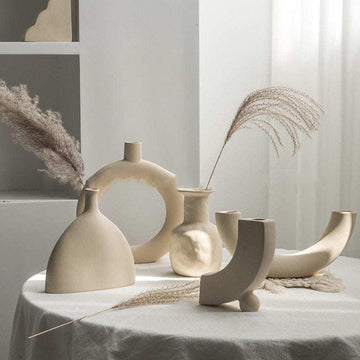 Minimalist ceramic vases in neutral tones on a white tablecloth, with dried grasses.