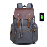 Grey canvas backpack with brown leather flap, multiple pockets, USB charging port, modern fit