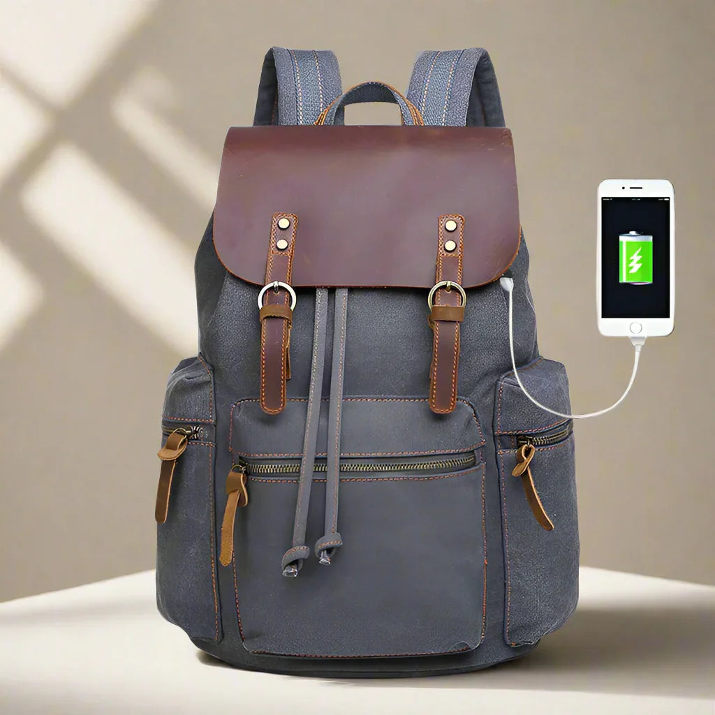 Gray canvas backpack with brown leather flap, multiple pockets, and USB charging port.