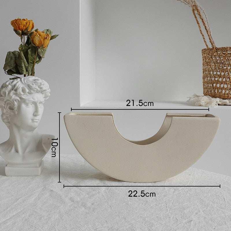 Minimalist beige ceramic vase with semi-circular shape on textured surface, home decor