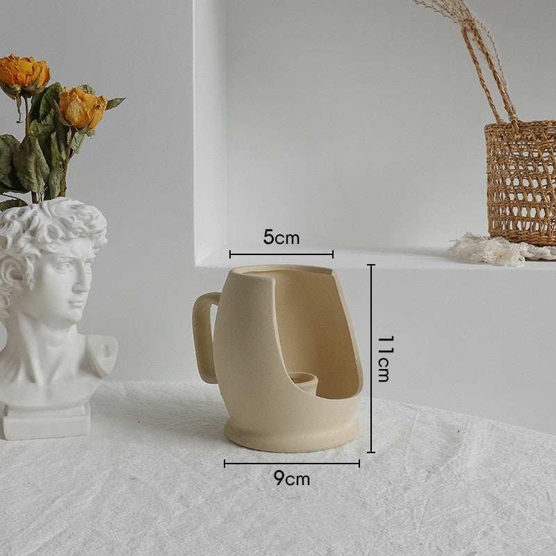 Beige ceramic mug with modern open design, rounded shape, and measurement labels, on fabric surface