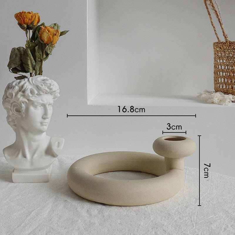 Minimalist beige ceramic circular vase with modern design, displayed on a white table near decor