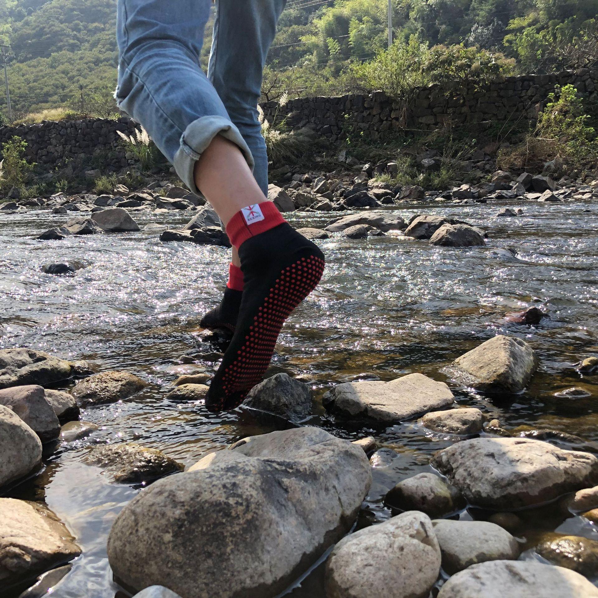 Person wearing black and red grip socks and rolled denim jeans stepping on river rocks outdoors