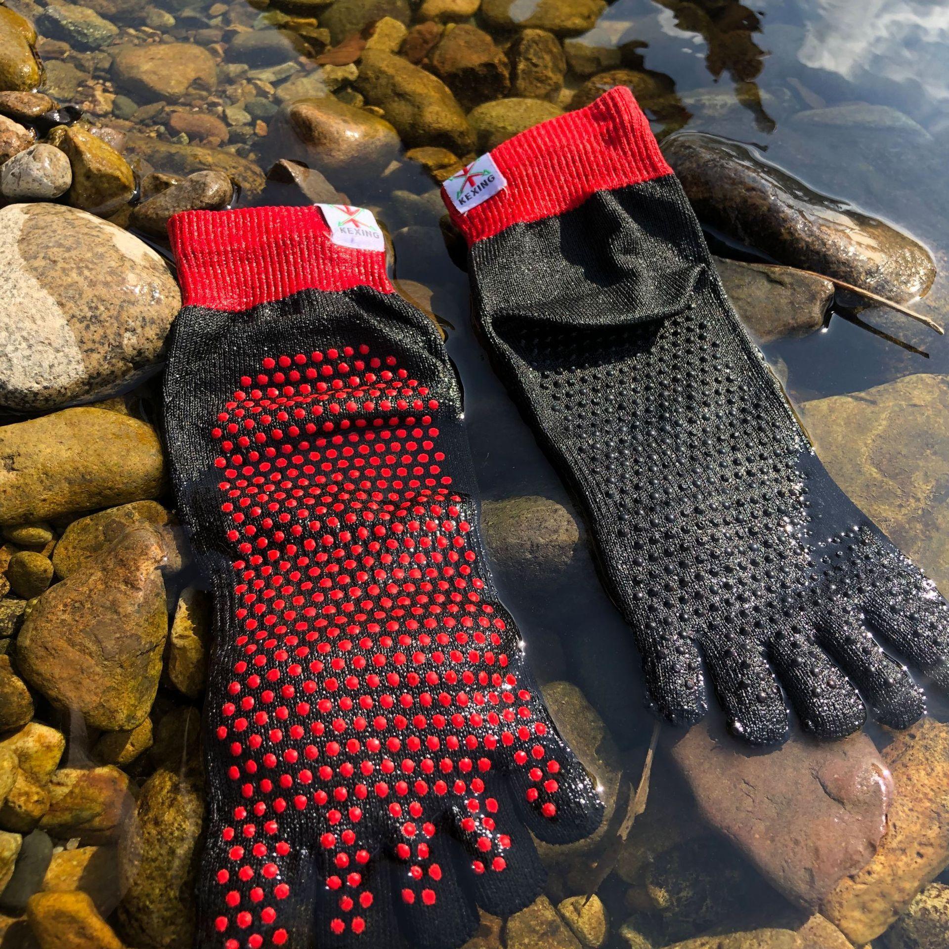Black five-toe water socks with red grip dots and red cuffs on rocky riverbank