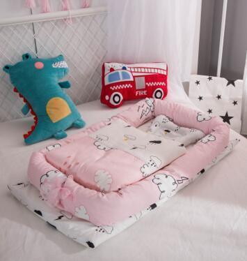 Pink baby nest bedding set with cloud pattern, soft cotton material, set on white bed with plush dinosaur and fire truck cushions.
