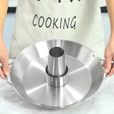Person wearing a beige apron holding a stainless steel roasting pan with cone center