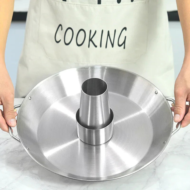 Person wearing a beige apron holding a stainless steel roasting pan with cone center