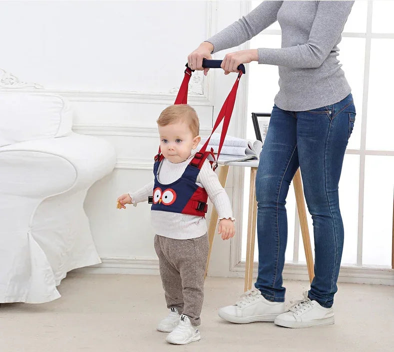 Toddler in navy blue and red walking harness vest with fun design, gray pants, knit sweater