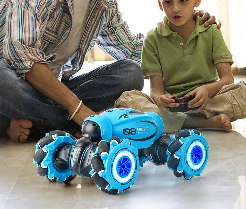 Boy in green polo shirt and adult in striped shirt playing with remote control blue robotic car indoors
