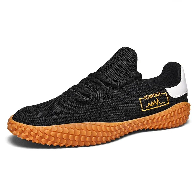 Black mesh streetwear sneaker with orange textured sole, white heel accent, and yellow side detail