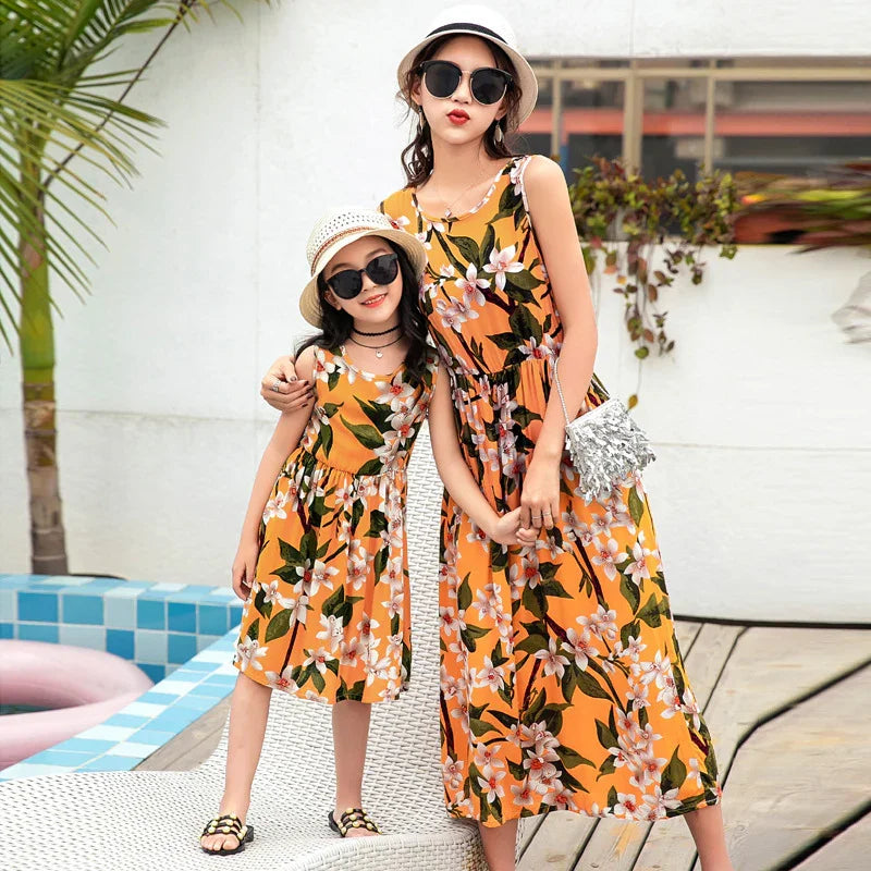 Mother and daughter in matching sleeveless orange floral dresses, relaxed fit, by poolside.