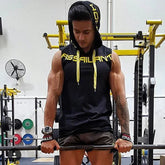Muscular man in a black sleeveless hoodie with yellow drawstrings, athletic fit, lifting weights in gym