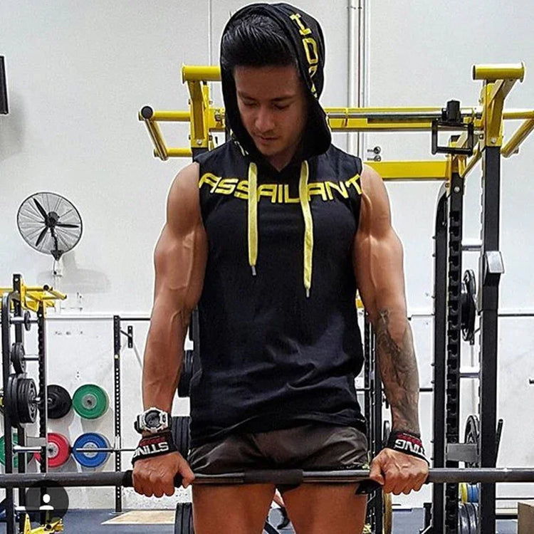 Muscular man in a black sleeveless hoodie with yellow drawstrings, athletic fit, lifting weights in gym