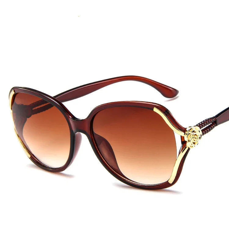 Oversized cat-eye sunglasses with brown gradient lenses, gold accents, and glossy plastic frame