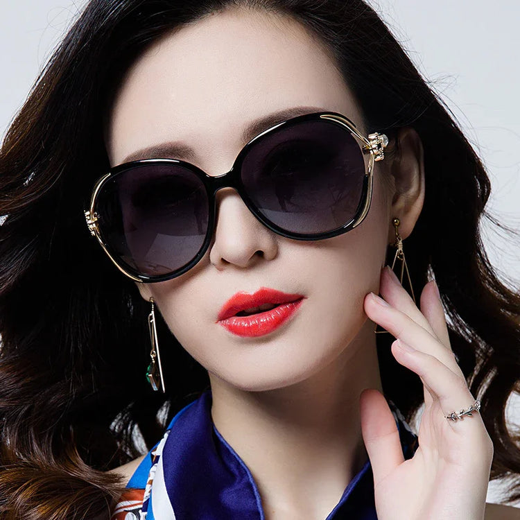 Woman wearing oversized round black sunglasses with gold accents, bold red lipstick, and a chic blue scarf