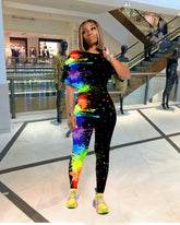 Woman wearing a fitted black jumpsuit with vibrant rainbow paint splatter print in a mall setting