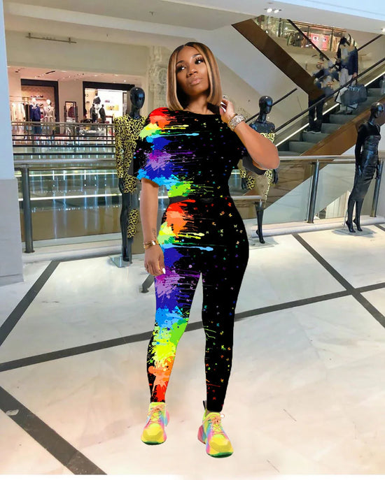 Woman wearing a fitted black jumpsuit with vibrant rainbow paint splatter print in a mall setting