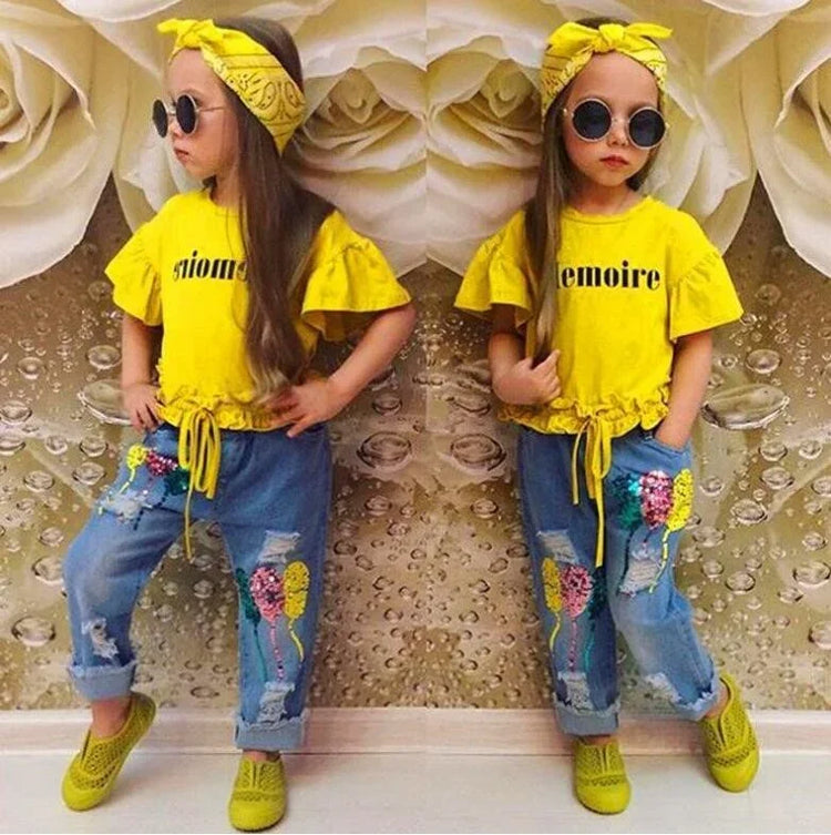 Girl in yellow ruffle sleeve shirt with drawstring, denim jeans with patches, and green shoes