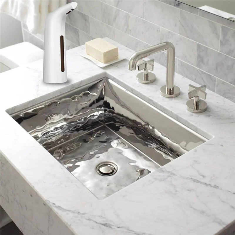 Modern bathroom with a rectangular stainless steel sink, marble countertop, chrome faucet, and touchless soap dispenser.