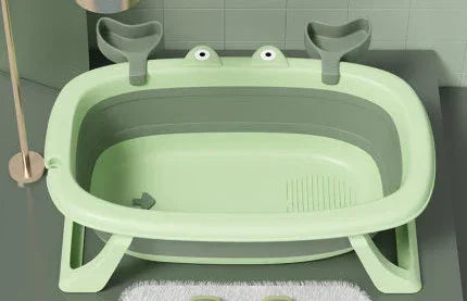 Light green plastic foldable baby bathtub with frog design and supportive backrest, set in a modern bathroom.