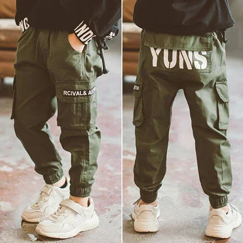 Child wearing olive green cargo jogger pants with side pockets, loose fit, and graphic text print