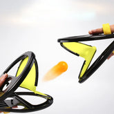 Two hands using yellow and black plastic toy catchers to toss an orange ball, action shot