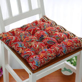 Red paisley-patterned cotton chair cushion with tufted design on a white wooden chair