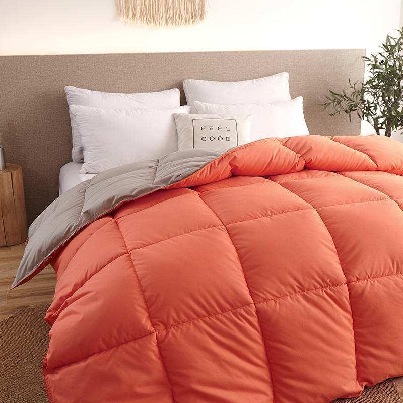 Modern bedroom with orange and gray quilted comforter, soft bedding, and decorative pillows