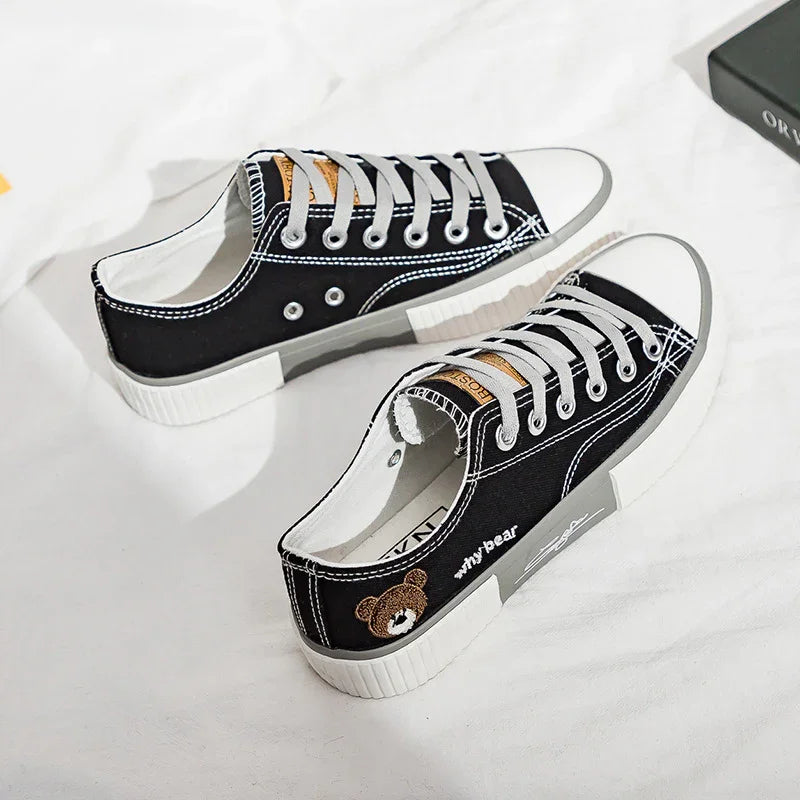 Black canvas low-top sneakers with white soles, grey laces, and bear patch detail.
