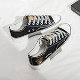 Black canvas low-top sneakers with white soles, grey laces, and bear patch detail.