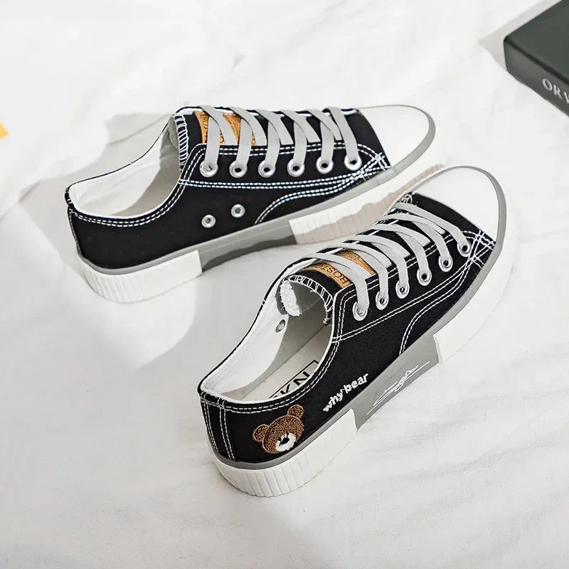 Black canvas low-top sneakers with white soles, grey laces, and bear patch detail.