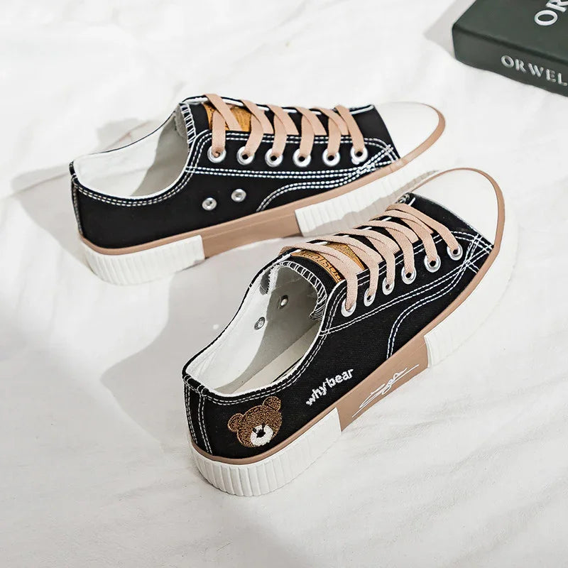 Black low-top canvas sneakers with tan rubber soles, beige laces, and embroidered teddy bear detail.