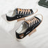 Black low-top canvas sneakers with tan rubber soles, beige laces, and embroidered teddy bear detail.