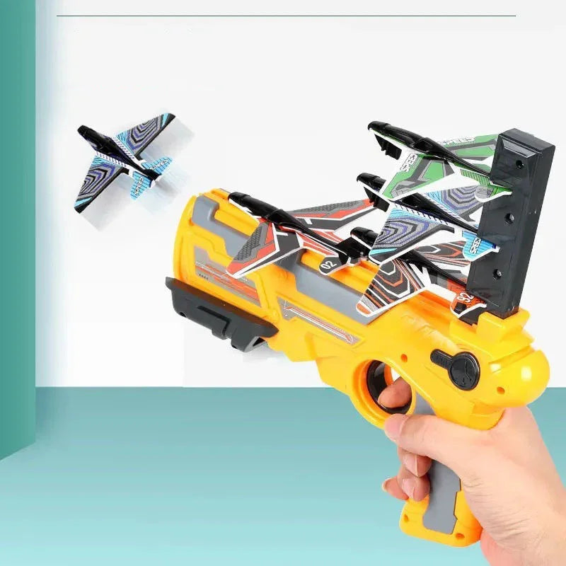 Hand holding a yellow toy launcher with colorful foam glider planes, one plane flying
