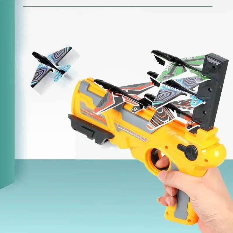 Hand holding a yellow toy launcher with colorful foam glider planes, one plane flying