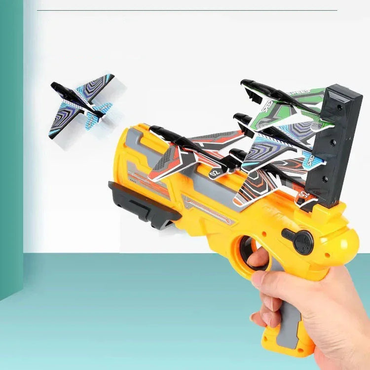 Hand holding a yellow toy launcher with colorful foam glider planes, one plane flying