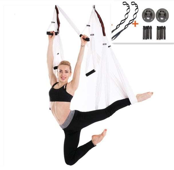 Woman in black crop top and leggings using white aerial yoga swing, demonstrating a split pose.