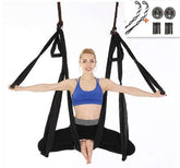 Woman wearing a blue sports bra and black leggings, demonstrating aerial yoga with a black hammock swing.