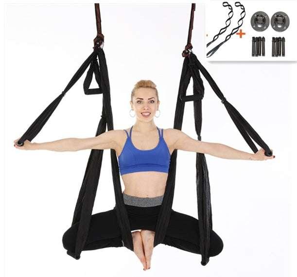 Woman wearing a blue sports bra and black leggings, demonstrating aerial yoga with a black hammock swing.