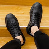 Black low-top sneakers with textured leather panels and a sleek, modern streetwear style fit.
