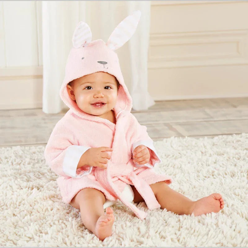 Baby in soft pink hooded robe with bunny ears, sitting on plush carpet